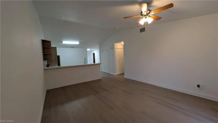 Empty room with dark wood-style flooring, vaulted ceiling, and ceiling fan