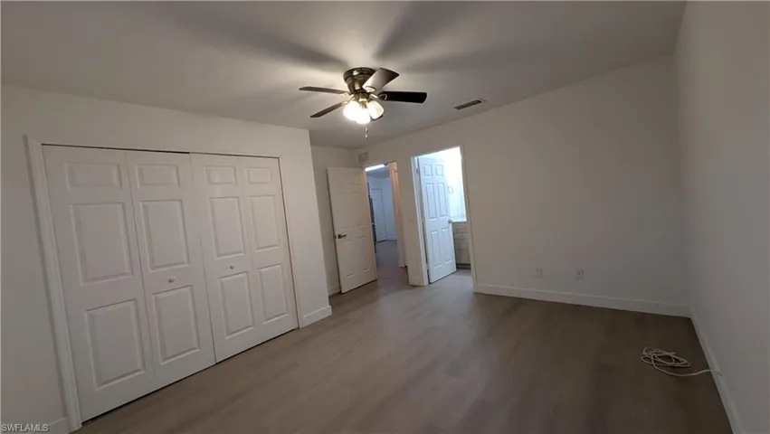 Unfurnished bedroom with wood finished floors, a closet, a ceiling fan, and ensuite bathroom