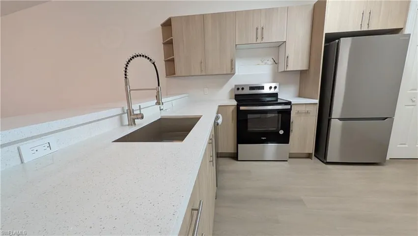 Kitchen featuring open shelves, appliances with stainless steel finishes, light brown cabinets, light stone countertops, and light wood-type flooring
