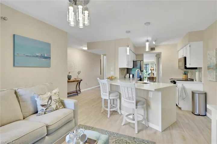Kitchen with white cabinetry, a kitchen breakfast bar, backsplash, open floor plan, and light stone counters