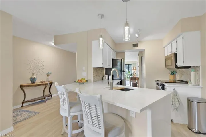 Kitchen with white cabinets, a kitchen bar, decorative backsplash, light wood-style floors, and a peninsula