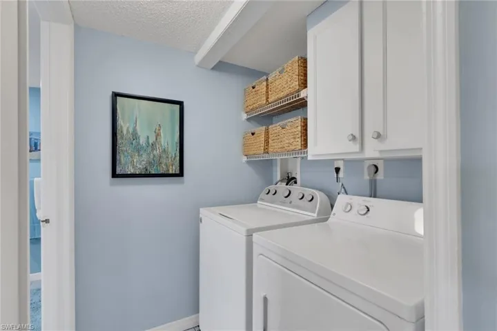 Washroom featuring a textured ceiling, washer and clothes dryer, and cabinet space