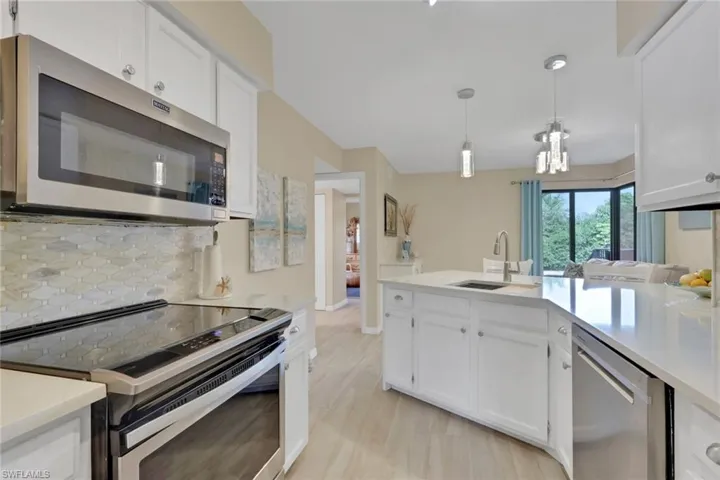Kitchen featuring stainless steel appliances, white cabinets, backsplash, pendant lighting, and light stone counters