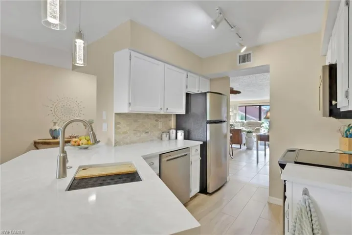 Kitchen featuring hanging light fixtures, white cabinets, dishwasher, track lighting, and backsplash