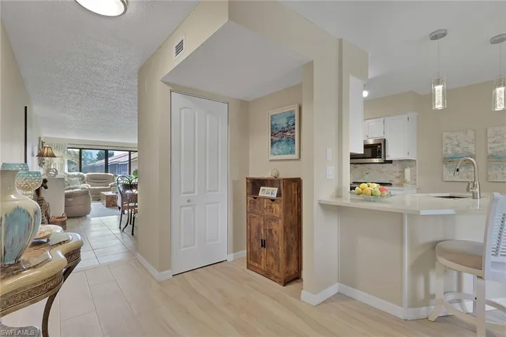 Kitchen featuring a breakfast bar, white cabinetry, decorative backsplash, pendant lighting, and stainless steel microwave