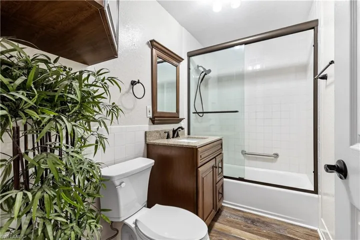 Full bathroom featuring tile walls, bath / shower combo with glass door, toilet, vanity, and wood-type flooring