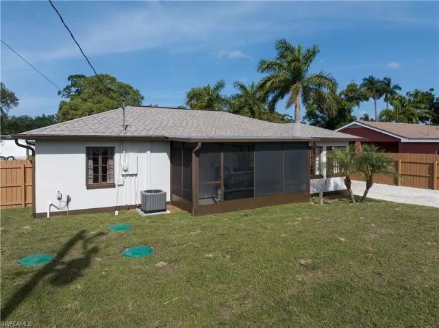 Rear view of house with a sunroom, central AC unit, and a lawn