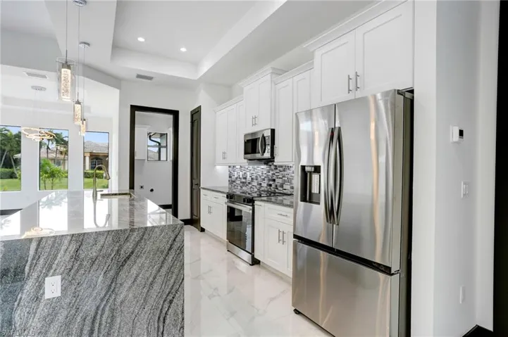 Kitchen featuring a raised ceiling, light stone countertops, appliances with stainless steel finishes, sink, and white cabinets