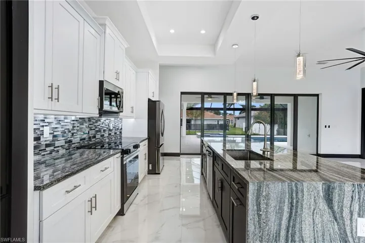 Kitchen with white cabinetry, backsplash, light tile patterned floors, stainless steel appliances, and a tray ceiling