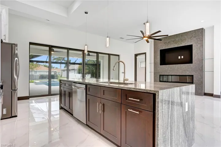 Kitchen featuring a large fireplace, light tile patterned floors, light stone counters, sink, and ceiling fan