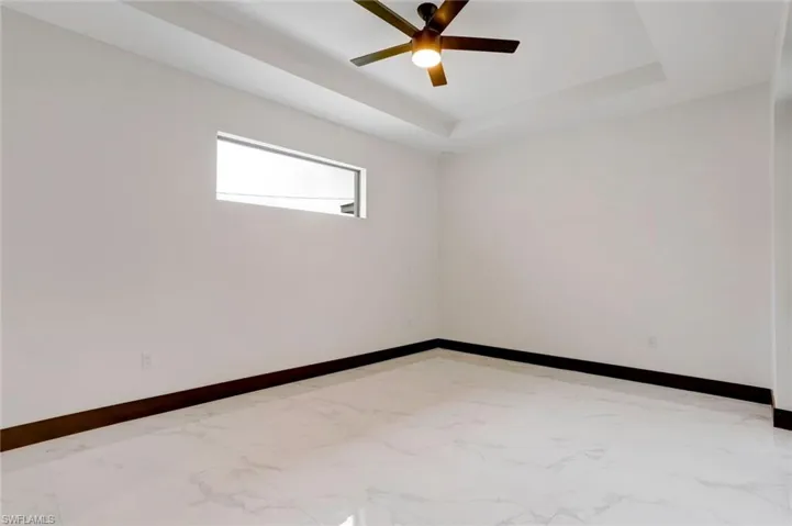 Tiled empty room featuring a tray ceiling and ceiling fan