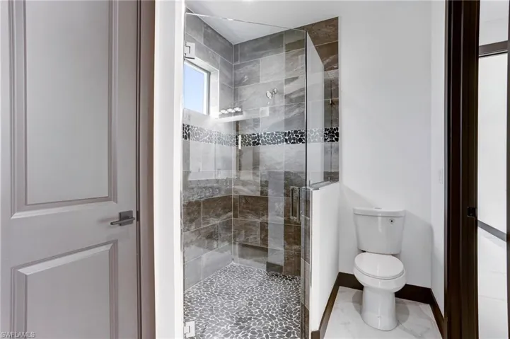 Bathroom featuring a shower with door, toilet, and tile patterned floors