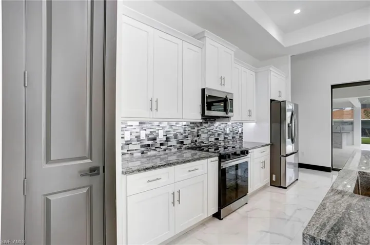 Kitchen with light tile patterned flooring, appliances with stainless steel finishes, white cabinetry, and stone counters