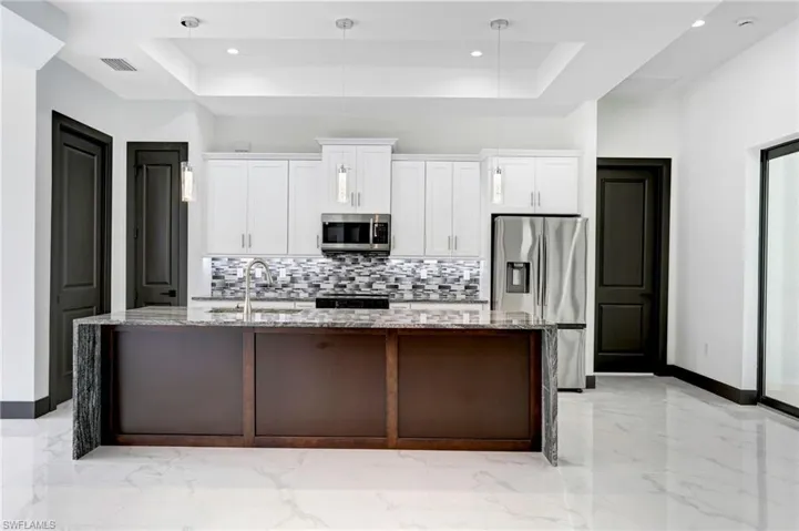 Kitchen featuring an island with sink, a raised ceiling, stainless steel appliances, and hanging light fixtures