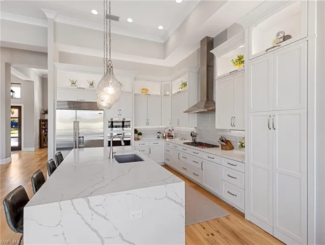Kitchen with sink, wall chimney range hood, pendant lighting, a center island with sink, and appliances with stainless steel finishes
