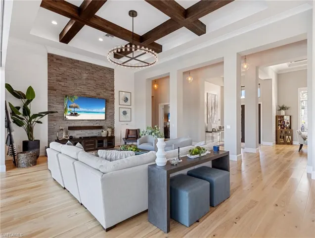 Living room featuring beam ceiling, light wood-type flooring, coffered ceiling, and an inviting chandelier