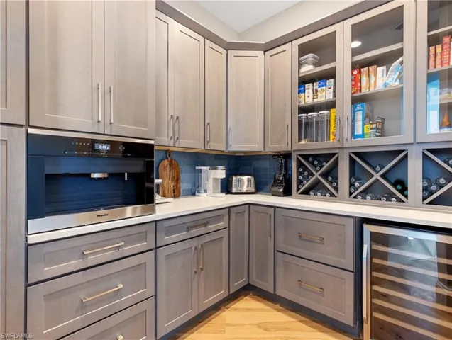 Butler's Pantry with gray cabinetry, beverage cooler, light hardwoodflooring, oven, and decorative backsplash