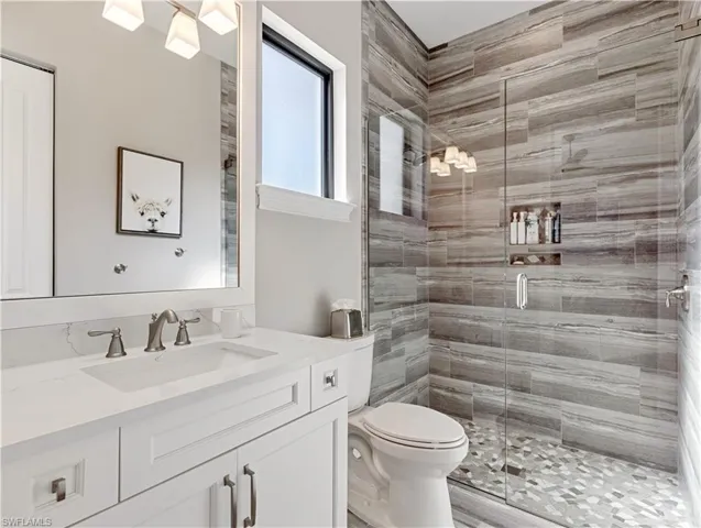 Bathroom featuring a shower with door, vanity, and toilet