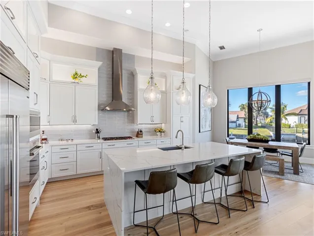 Kitchen with tasteful backsplash, wall  exhaust hood, a kitchen island with sink, sink, and white cabinets