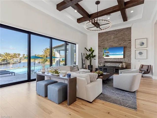 Living room featuring beam ceiling, coffered ceiling, a notable chandelier, light hardwood floors, and a water view