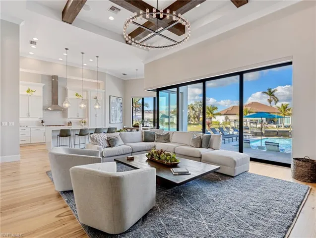 Living room with beamed ceiling, a towering ceiling, light wood flooring, and a notable chandelier