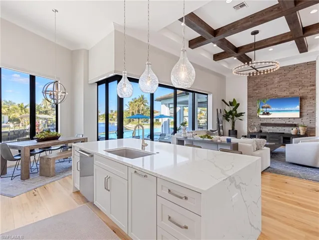 Kitchen featuring decorative light fixtures, white cabinetry, a center island with sink, and sink