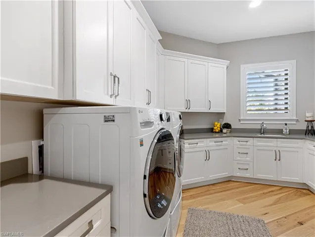 Clothes washing area featuring washer and dryer, cabinets, light wood-type flooring, and sink