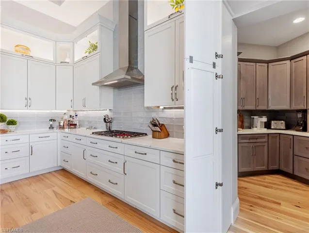 Kitchen featuring white cabinets, tasteful backsplash, stainless steel gas stovetop, and wall  range hood
