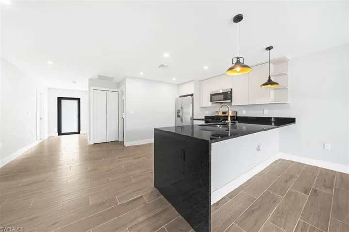 Kitchen featuring an island with a stone countertop, cabinetry with light finish, recessed lighting, industrial-style pendant fixtures, and wood-finish tile flooring