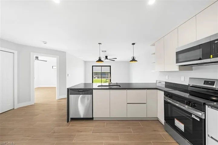Kitchen featuring flat-panel cabinetry, dark stone-finish countertops, stainless steel appliances, dual pendant lighting, and wood-finish flooring