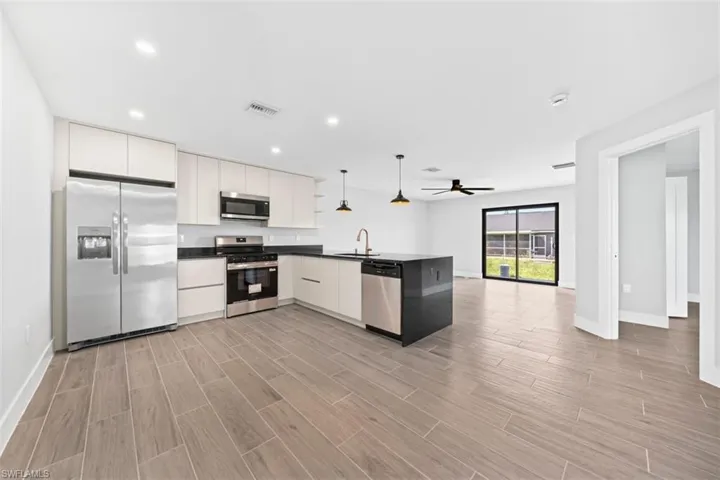 Kitchen featuring flat-panel cabinetry, dark stone-finish countertops, stainless steel appliances, wood-finish flooring, and a kitchen island with integrated lighting