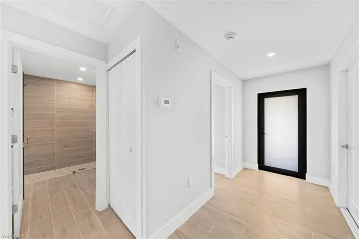 Interior hallway featuring wood-finish tile flooring, recessed lighting, and a modern door with a frosted glass panel and black frame