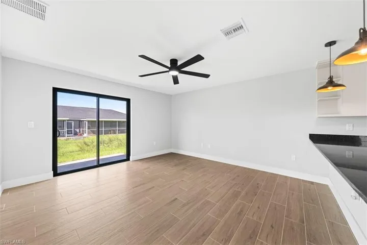 Open-concept area featuring wood-finish tile flooring, a matte black ceiling fan, sliding glass doors, and a kitchen counter with dark stone-finish surfaces and pendant lighting