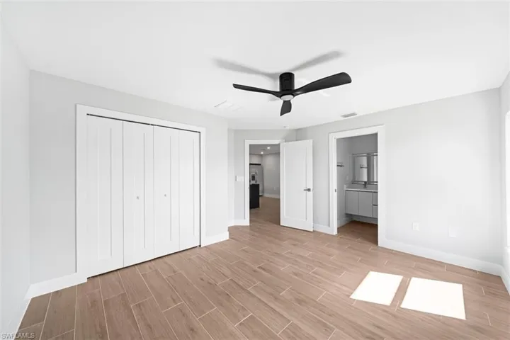 Neutral interior featuring wood-finish flooring, a matte black ceiling fan, and white bifold closet doors