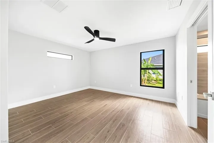 Neutral-toned room featuring wood-finish flooring, a sleek black ceiling fan, and black-framed windows including a horizontal transom