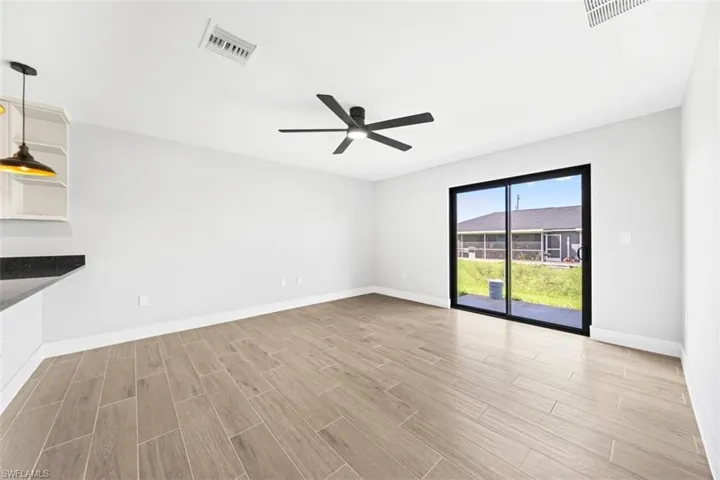 Open-concept area featuring wood-finish flooring, a matte black ceiling fan, and sliding glass doors leading to the exterior