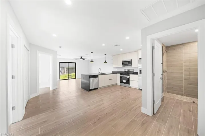 Kitchen featuring flat-panel cabinetry, a center island with a dark countertop, stainless steel appliances, wood-finish tile flooring, and a walk-in shower with textured wall tile