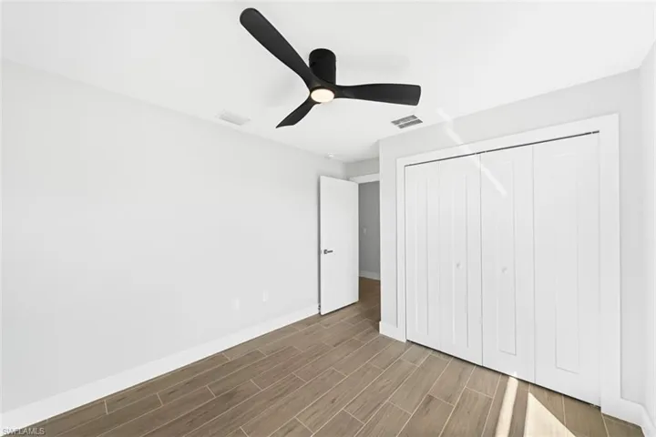Room featuring wood-finish flooring, matte black three-blade ceiling fan with integrated light, and white paneled bi-fold closet doors