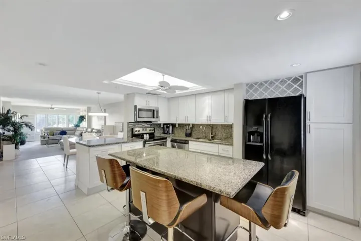 Kitchen featuring stainless steel appliances, ceiling fan, a peninsula, light stone counters, and a kitchen breakfast bar