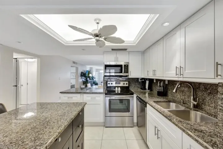 Kitchen with a tray ceiling, white cabinets, stainless steel appliances, dark stone counters, and recessed lighting
