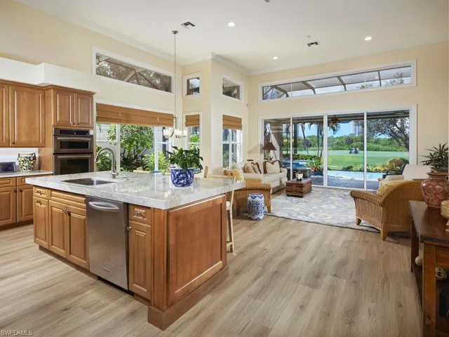 Kitchen with light hardwood / wood-style floors, a high ceiling, a kitchen island with sink, and decorative light fixtures