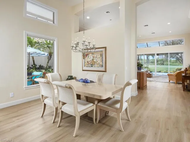 Dining room with a towering ceiling, light hardwood / wood-style floors, a chandelier, and a healthy amount of sunlight