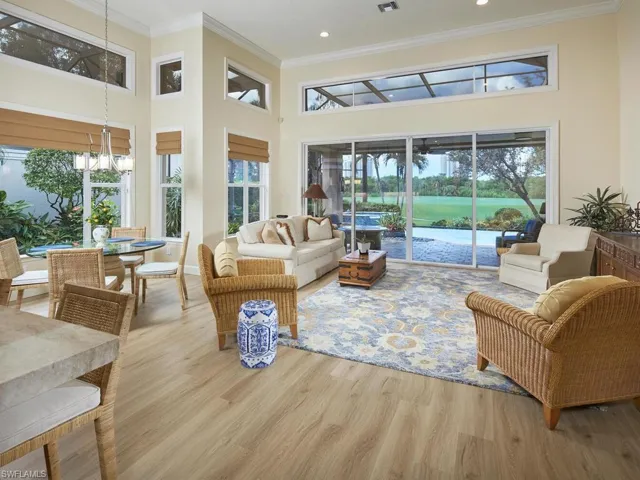 Living room with light hardwood / wood-style flooring, a towering ceiling, crown molding, and a healthy amount of sunlight