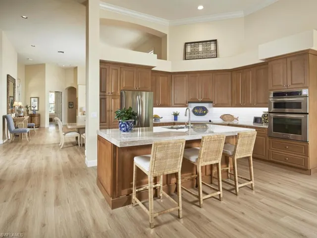 Kitchen with a towering ceiling, an island with sink, stainless steel appliances, crown molding, and light hardwood / wood-style flooring