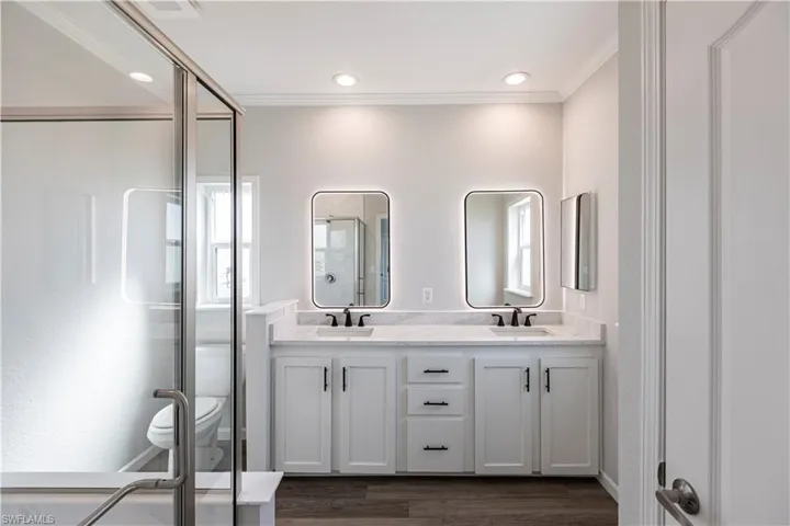 Full bath with a shower stall, double vanity, dark wood-style floors, and crown molding