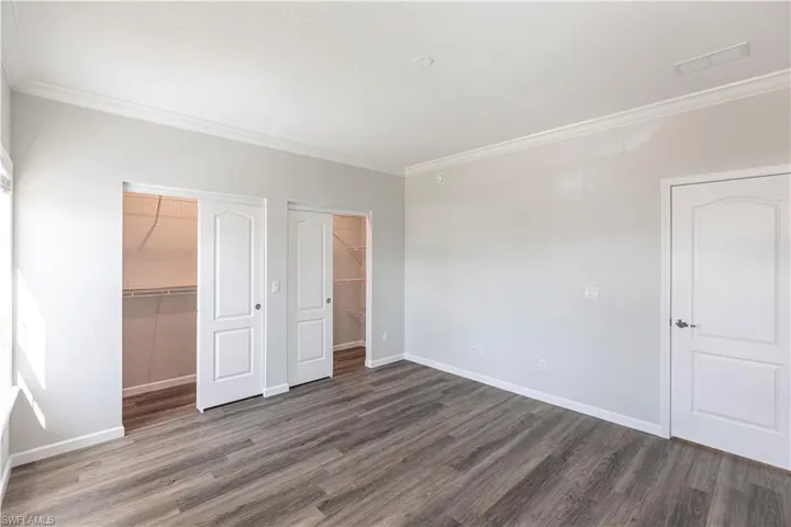 Unfurnished bedroom featuring crown molding, dark wood-type flooring, and multiple closets