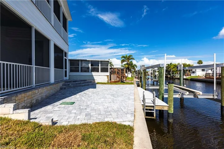 Dock with a sunroom, boat lift, a water view, and a patio