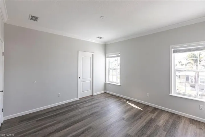 Empty room with crown molding and dark wood-style flooring