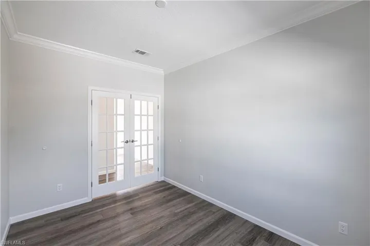 Empty room with french doors, crown molding, and dark wood-style floors