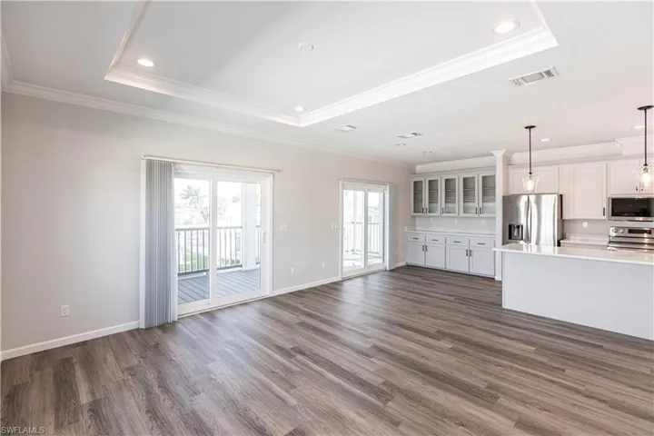 Unfurnished living room featuring recessed lighting, dark wood-style flooring, ornamental molding, and a tray ceiling